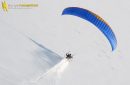 Vue aérienne d'un paramoteur volant à basse altitude et laissant une traînée dans la neige