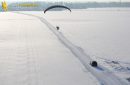 Vue aérienne du parapente motorisé survolant une route enneigée suivie d'une voiture