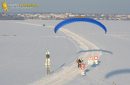 Vue aérienne d'un paramoteur survolant une route enneigée avec panneau de limitation de vitesse